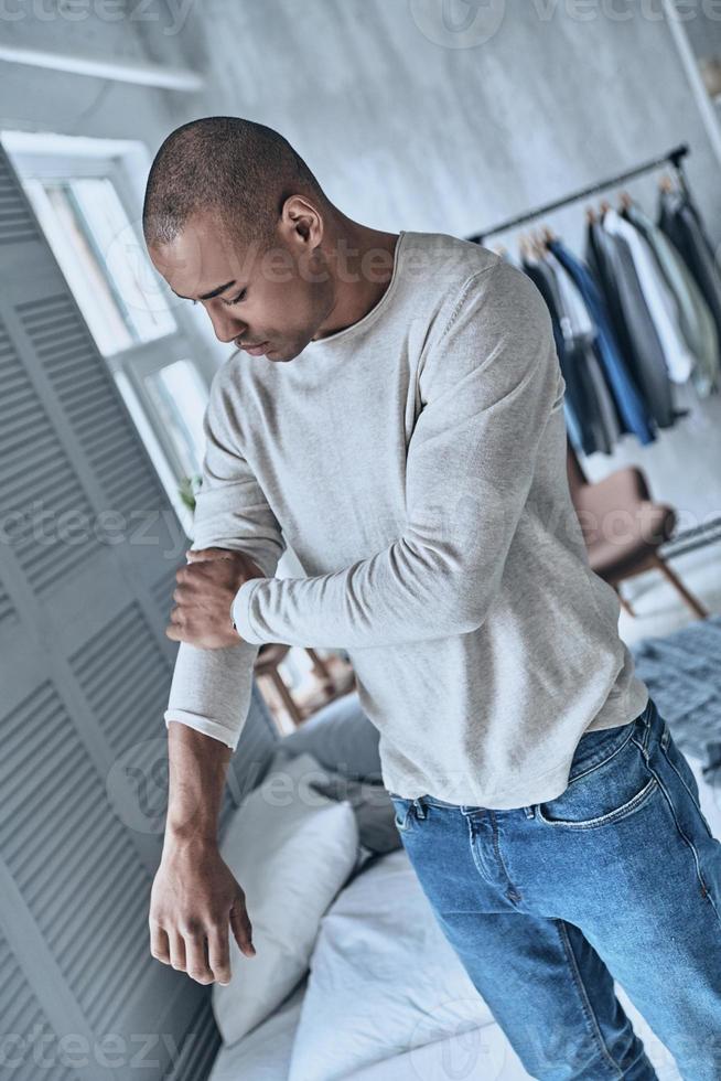 Finally ready to go. Top view of handsome young African man adjusting his sleeve while standing in the bedroom at home photo