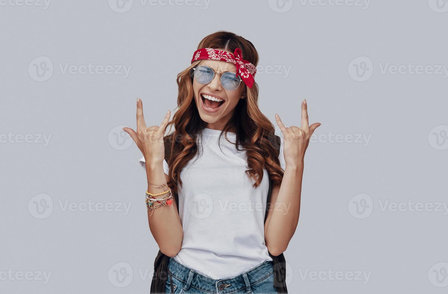 mujer joven atractiva y elegante haciendo una cara y gesticulando mientras está de pie contra el fondo gris foto