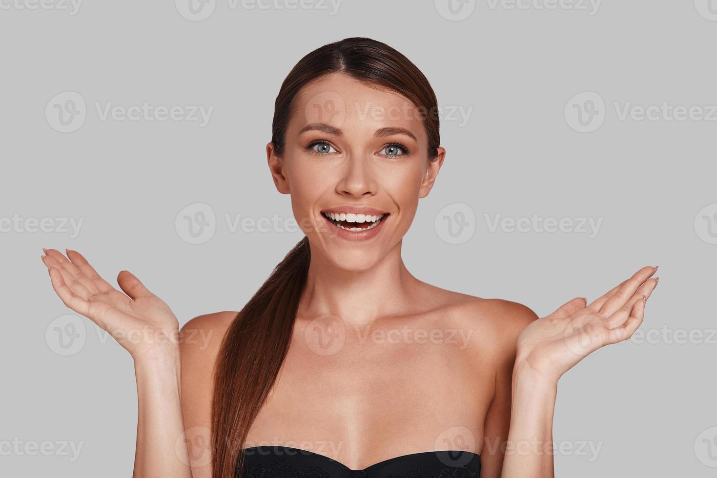Beautiful woman. Attractive young woman looking at camera and gesturing while standing against grey background photo