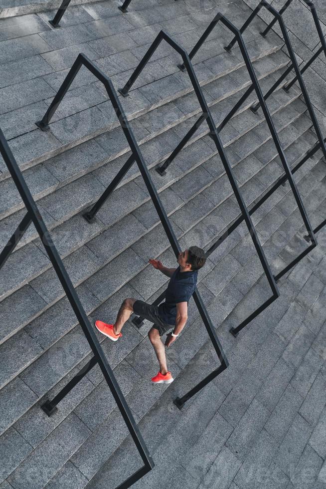 Giving all his best. Top view of young man in sports clothing running up the stairs while exercising outside photo