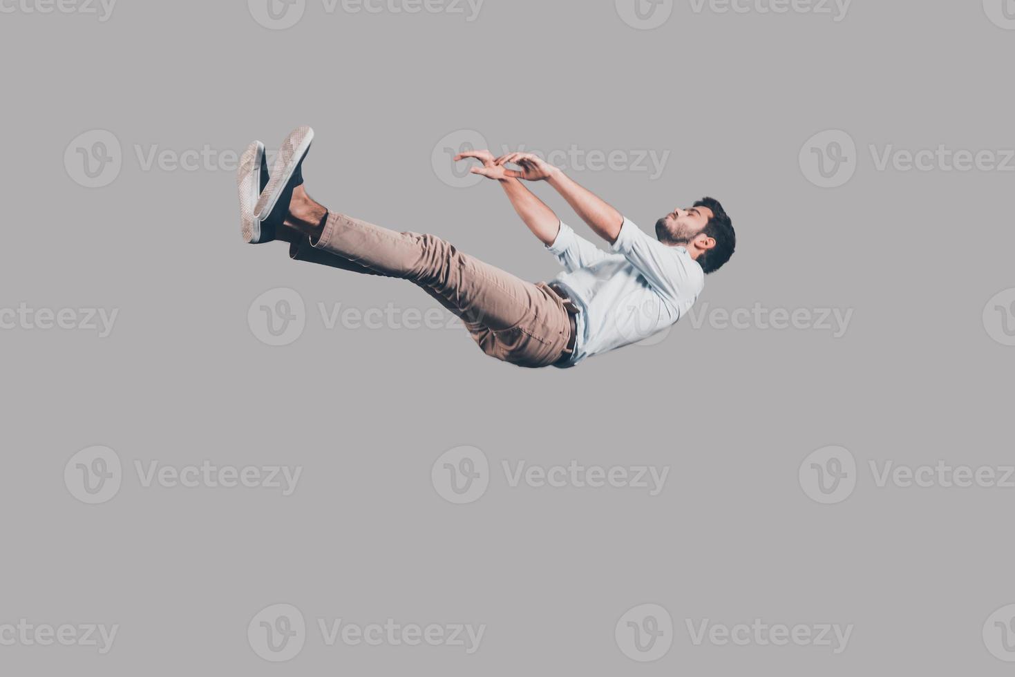 Just falling down. Mid-air shot of handsome young man falling against grey background photo