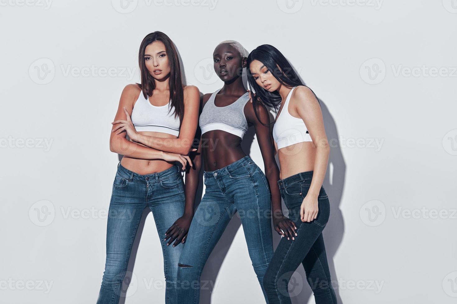 Every woman is a mystery. Three attractive young women looking at camera while standing against grey background photo