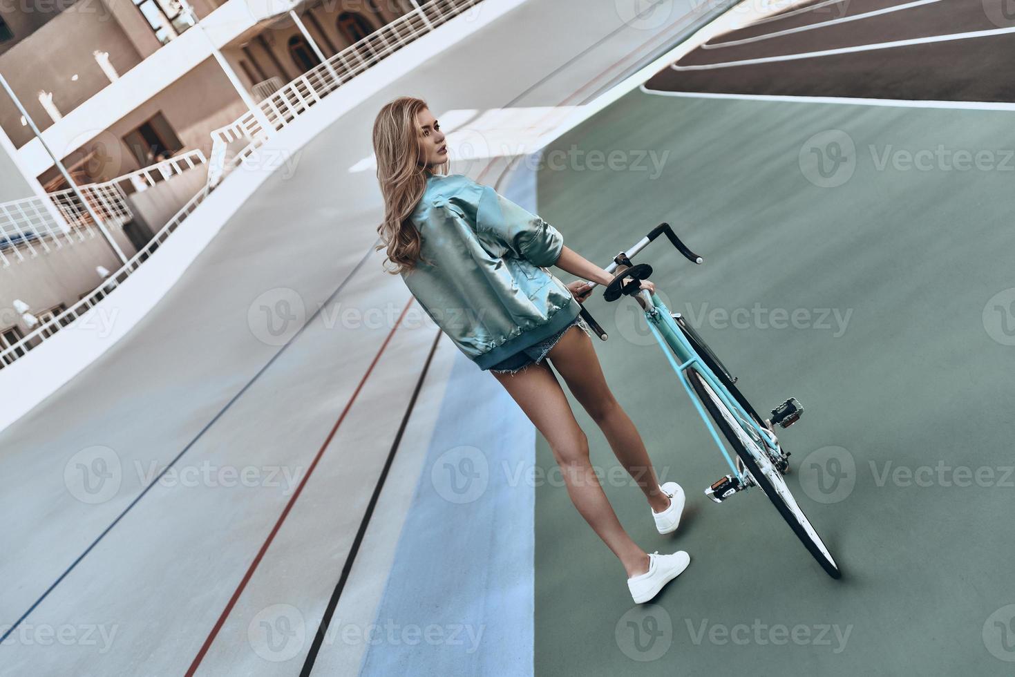 Time for some rest. Full length rear view of attractive young woman in casual clothing looking away while walking with her bicycle outdoors photo