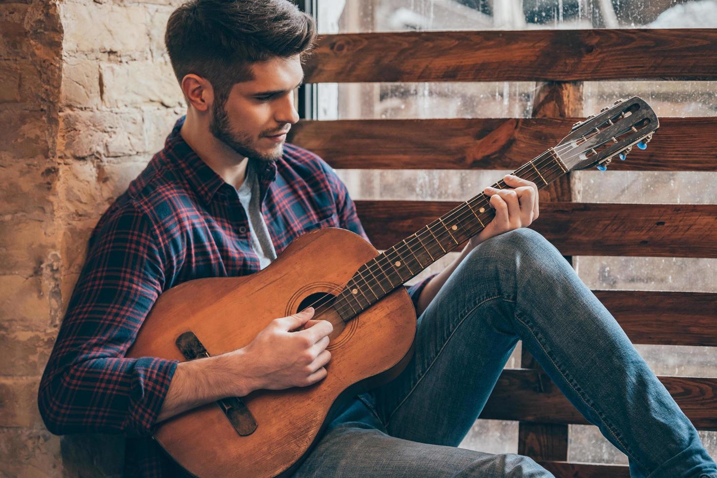 Talented guitarist. Handsome young man playing guitar while sitting at windowsill 13505593 Stock