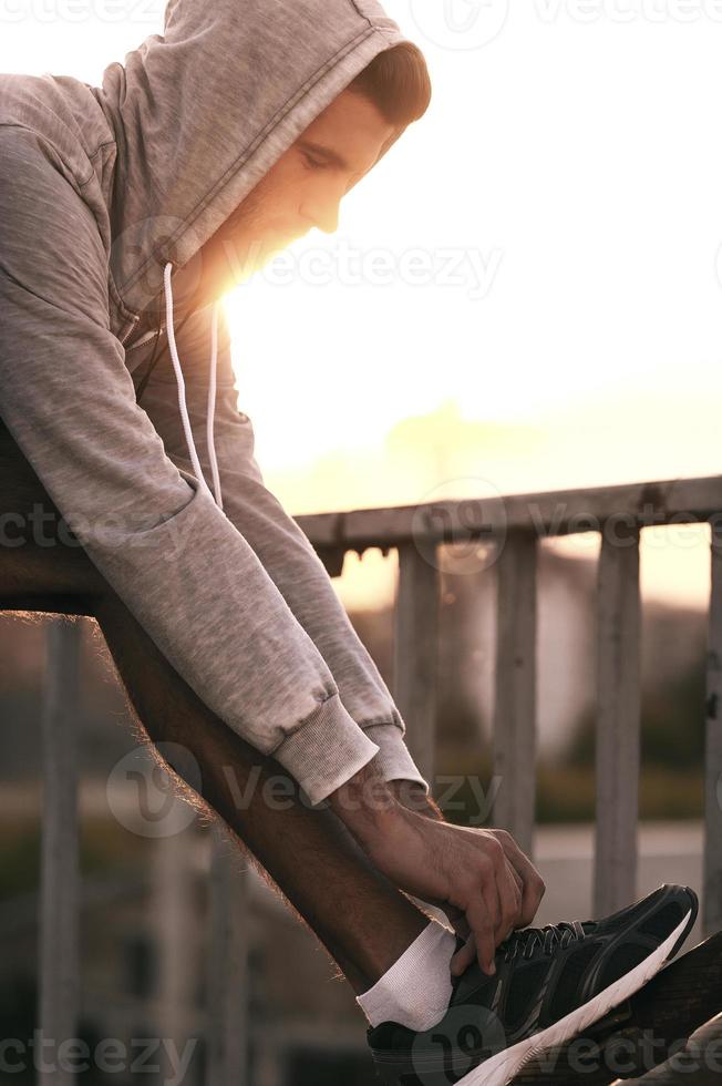 Preparing to run. Close-up of man tying shoelaces on sports shoe while standing outdoors photo