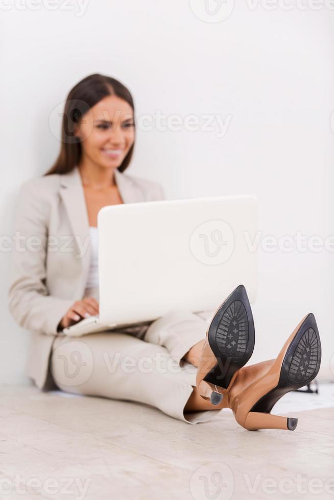 Having freedom to work everywhere. Beautiful young businesswoman working on laptop and smiling while sitting on the floor photo