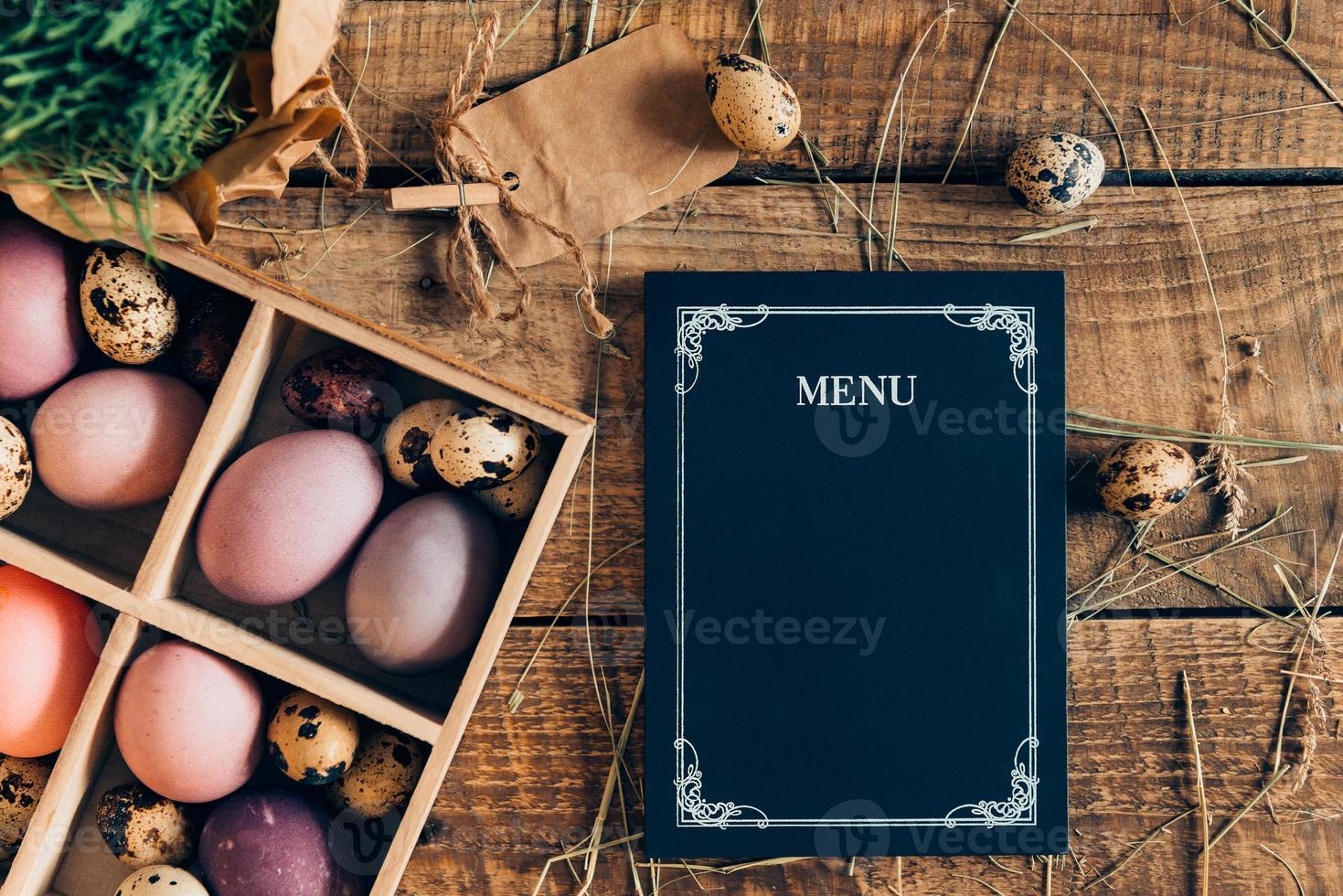 Easter menu. Top view of Easter eggs in wooden box and menu board lying on wooden rustic table with hay photo