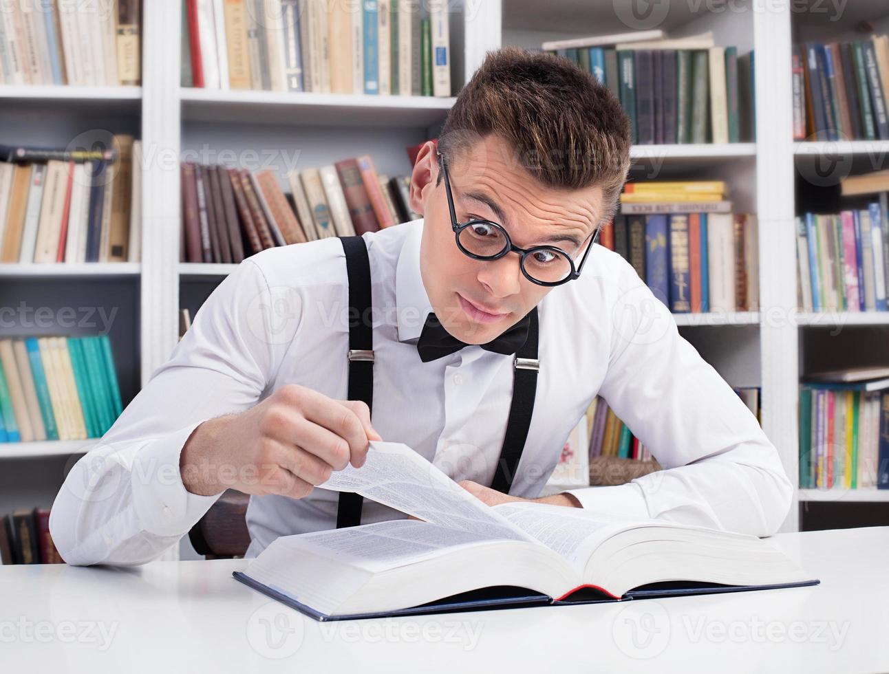 Shocking discovery. Surprised young man in shirt and bow tie reading a book in library photo