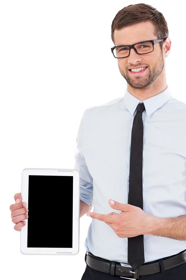 Copy space on his tablet. Cheerful young man in shirt and tie pointing digital tablet and smiling while standing isolated on white background photo