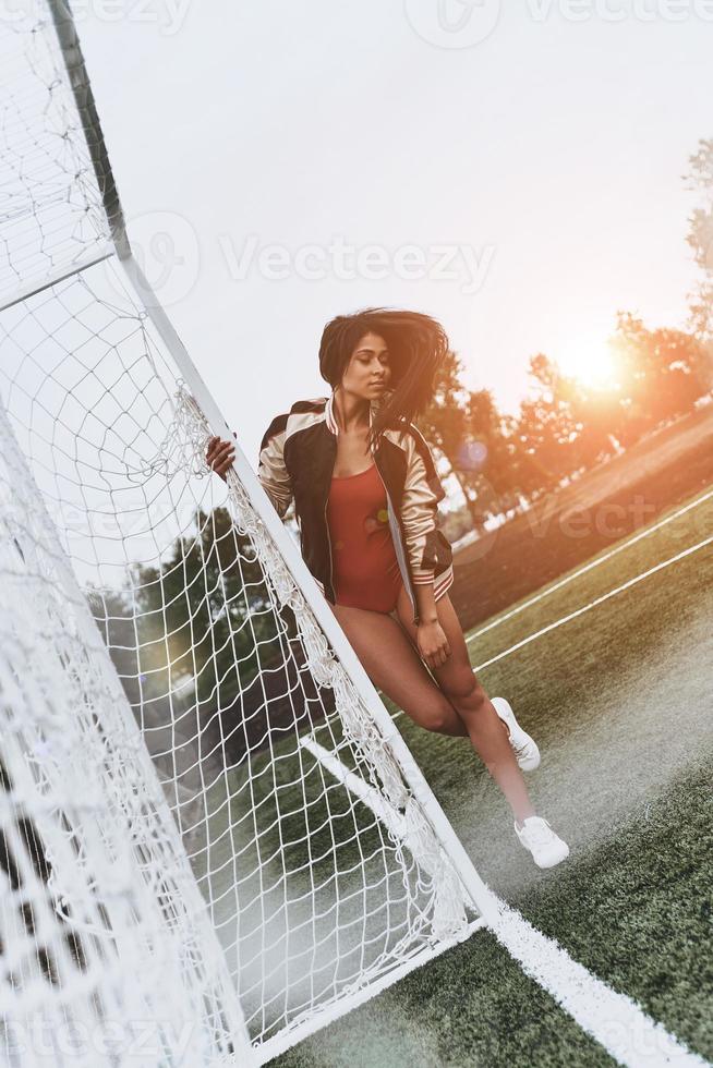 hermoso futbolista. toda la longitud de una joven atractiva en bikini rojo posando cerca del poste de gol en el campo de fútbol foto