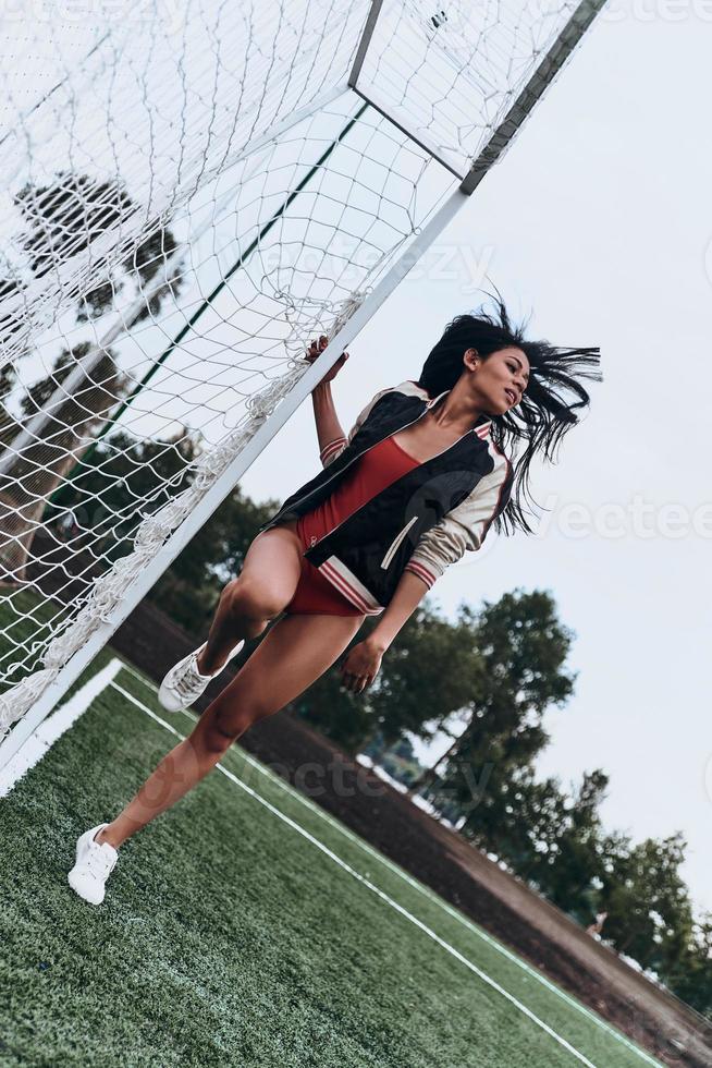 hermoso jugador toda la longitud de una joven atractiva en bikini rojo posando cerca del poste de gol en el campo de fútbol foto