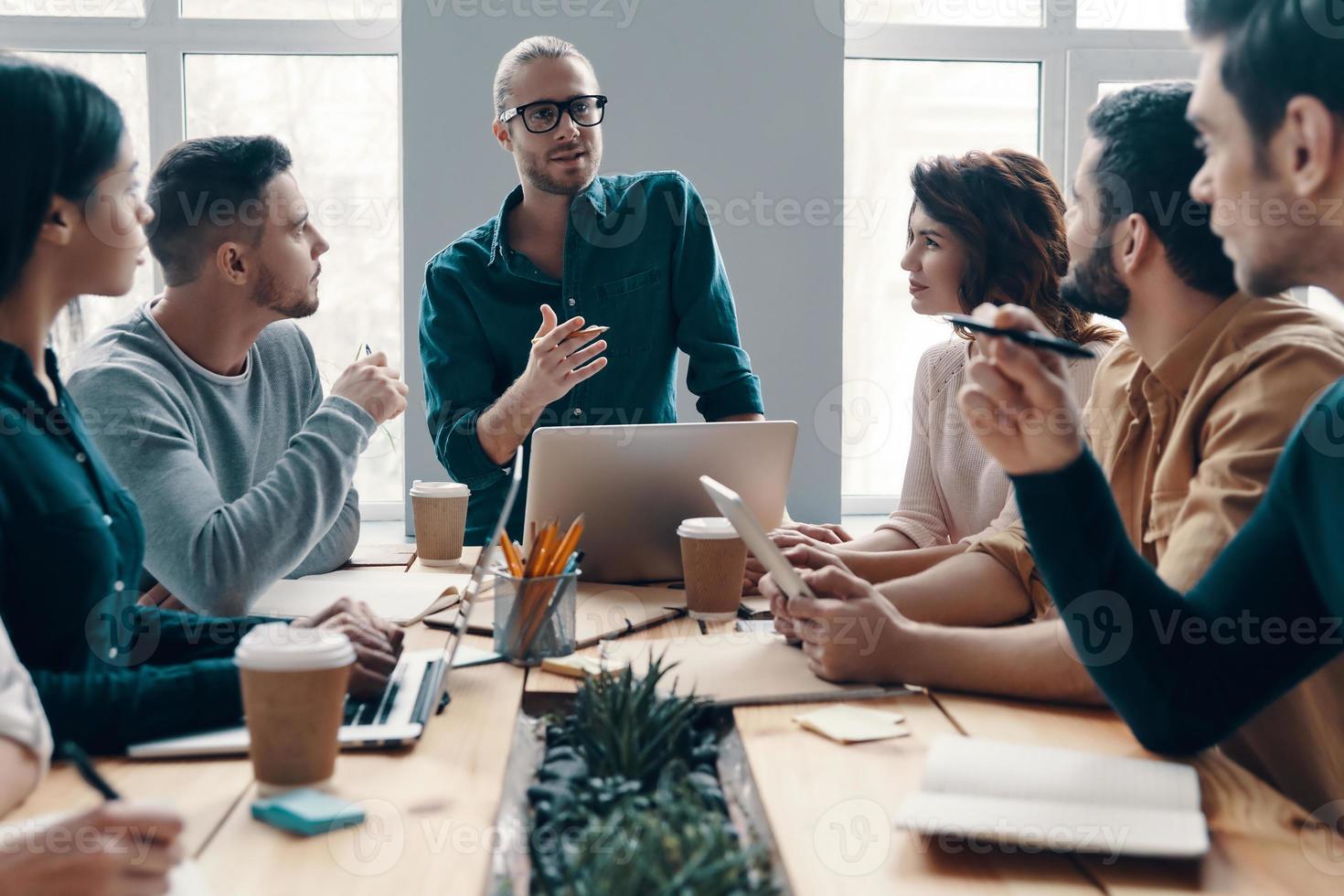 Planning new business strategy. Group of young modern people in smart casual wear discussing something while working in the creative office photo