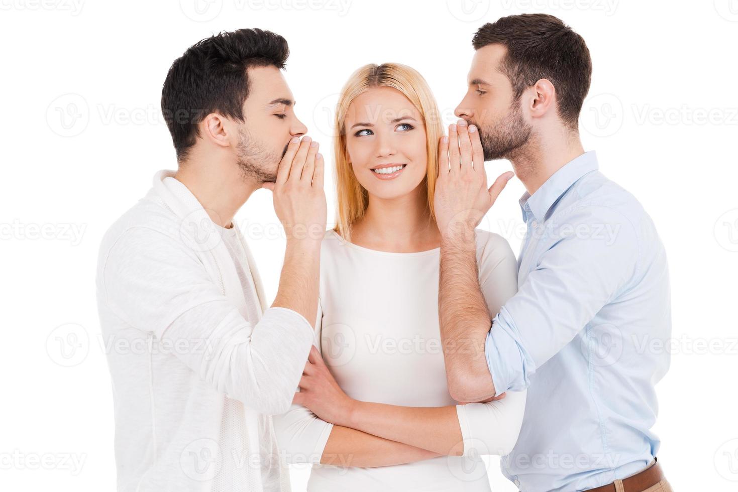 contando chismes frescos. dos jóvenes contando chismes a una mujer hermosa parada entre ellos y contra fondo blanco foto