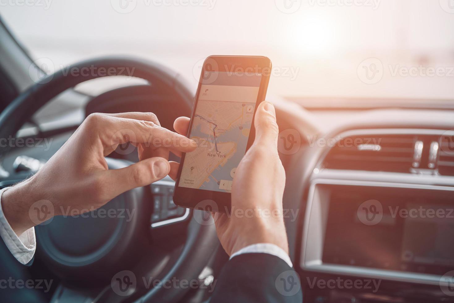 Checking the direction. Close up of young man using smart phone to check the map while driving a car photo