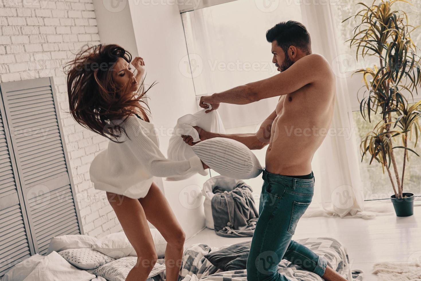 solo por diversión. feliz pareja joven teniendo una divertida pelea de almohadas mientras pasa tiempo sin preocupaciones en el dormitorio foto