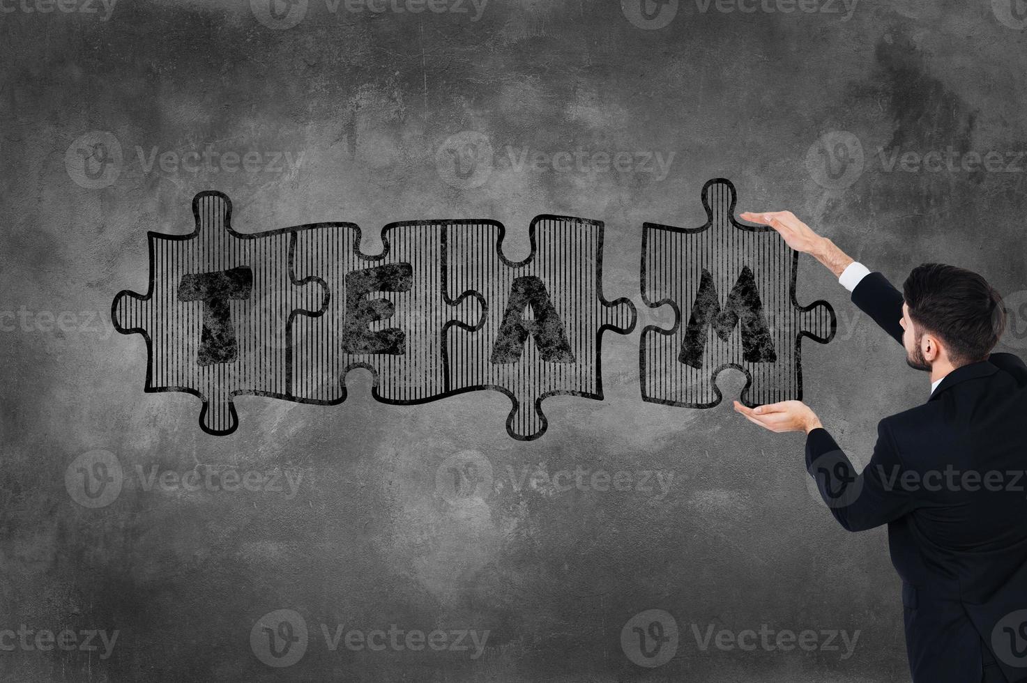 Be the team Rear view of young man in full suit touching concrete wall with illustrated puzzle on it photo