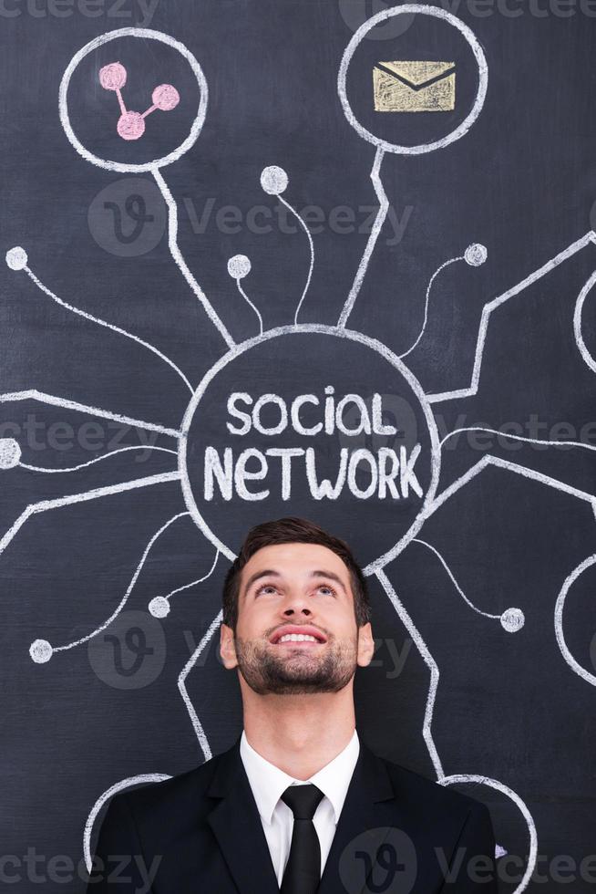 Social network. Handsome young man standing under social network chalk drawing on blackboard and looking up photo