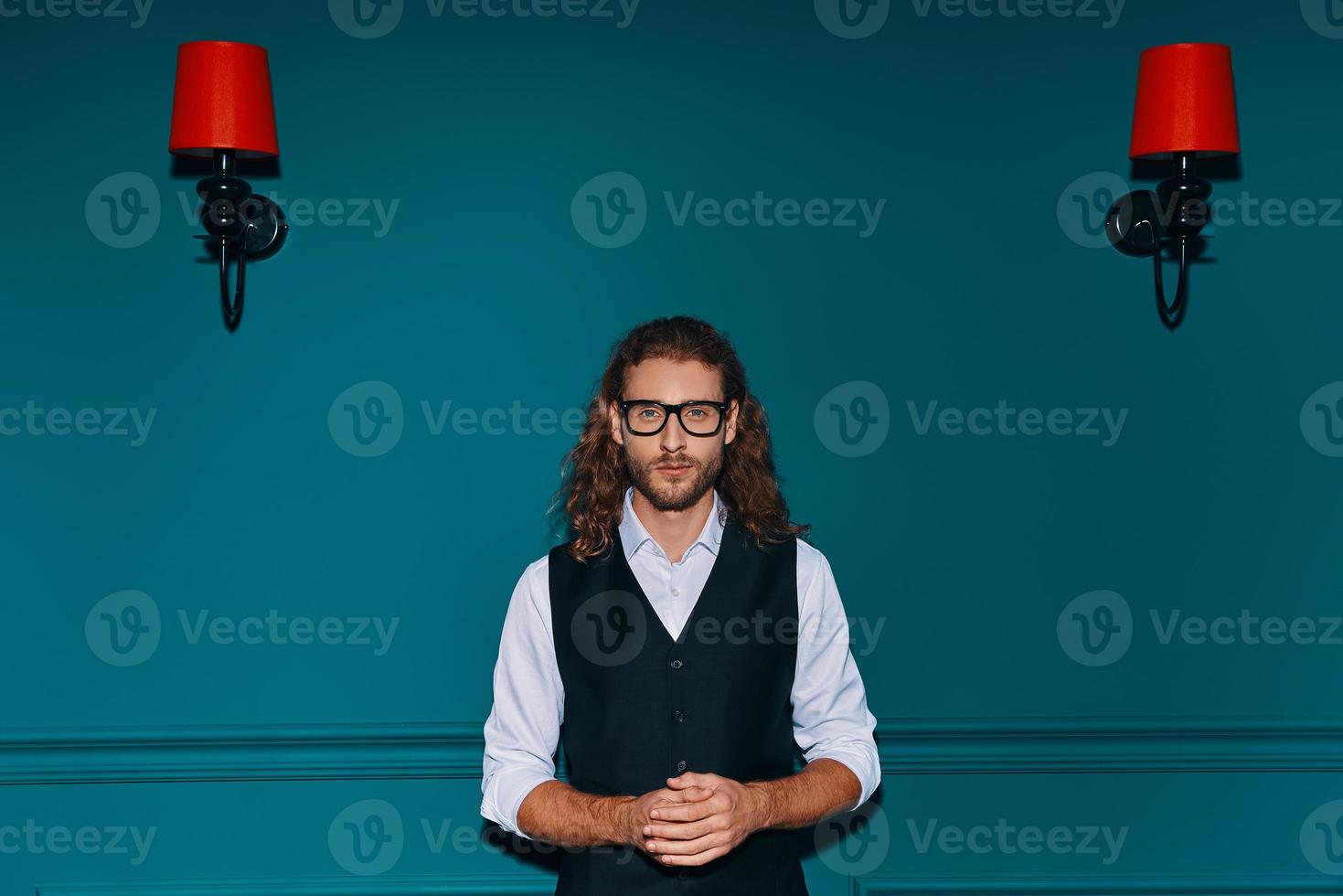 Stylish young man in elegant shirt looking at camera while standing against green background photo