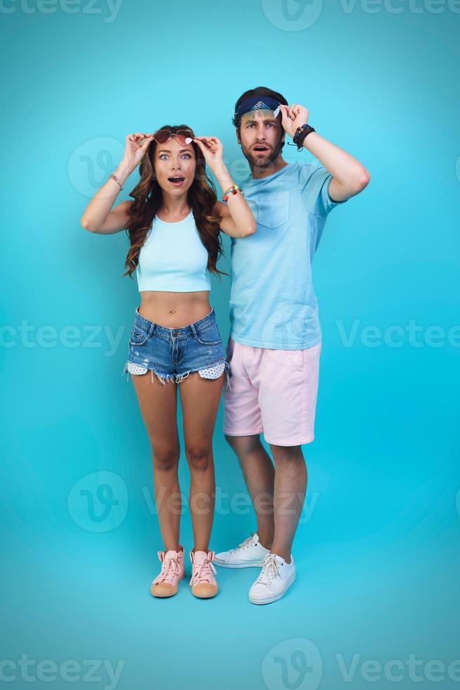 Full length of surprised young couple looking at camera while standing against blue background photo