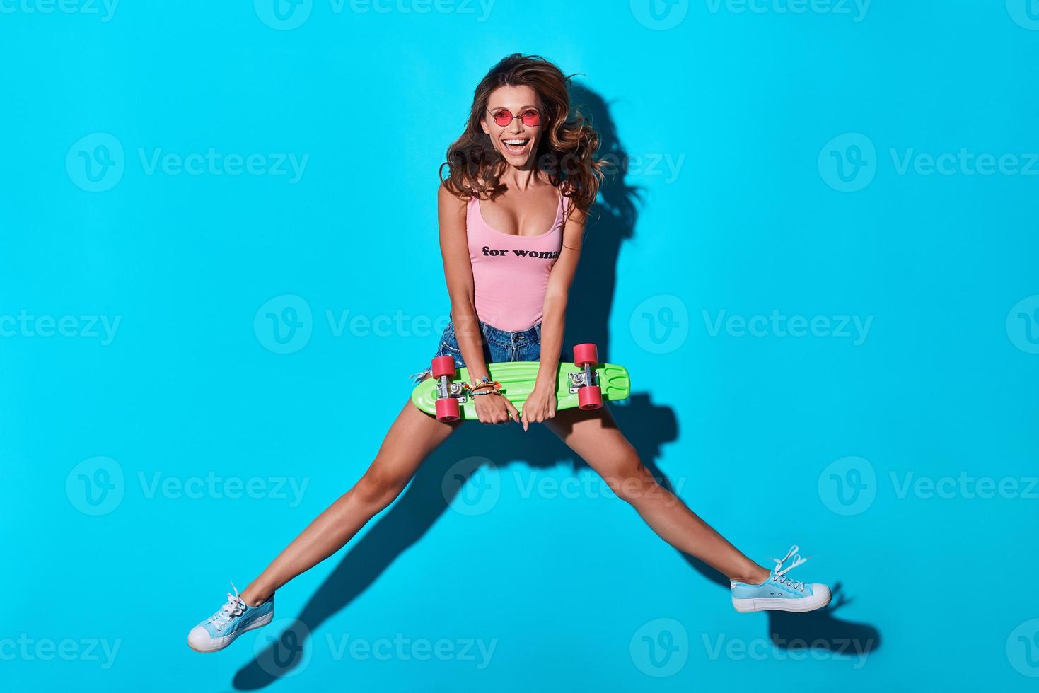 Mid-air fun. Full length of playful young woman smiling and looking at camera while hovering against blue background photo