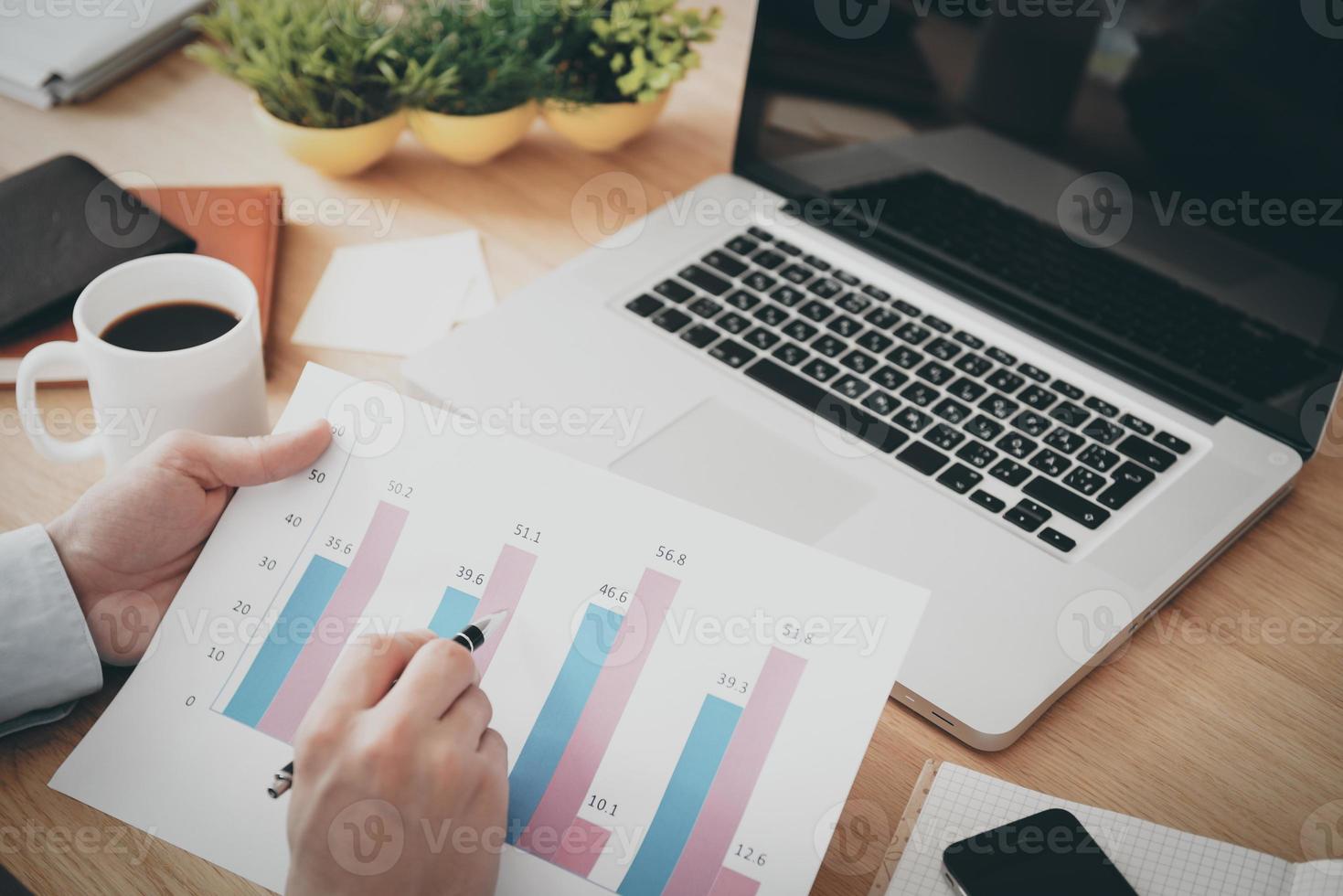 Looking at the company progress. Close-up top view of man holding paper with diagram on it while sitting his working place photo