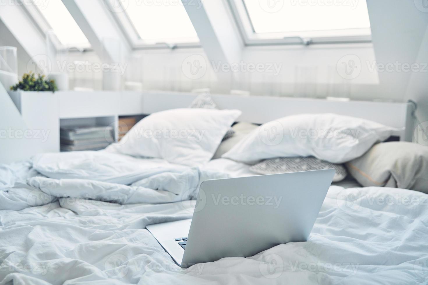 Image of laptop laying on bed with pillows and nanket around photo