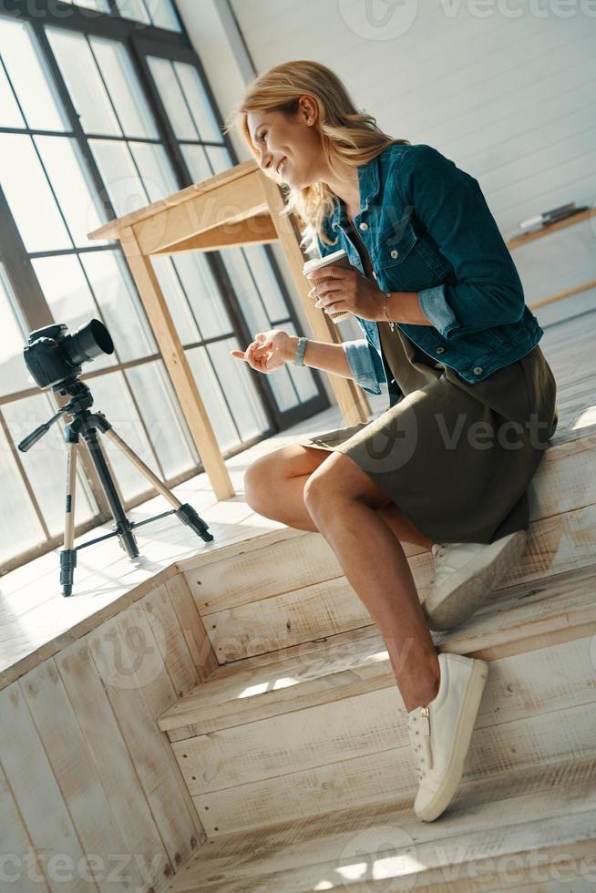 Beautiful young woman in casual clothing smiling while working in front of digital camera photo