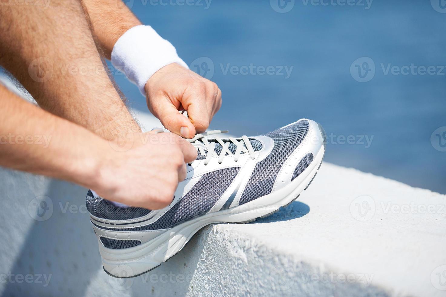 Tying shoelaces. Close-up of man tying shoelaces on sports shoe while standing outdoors photo
