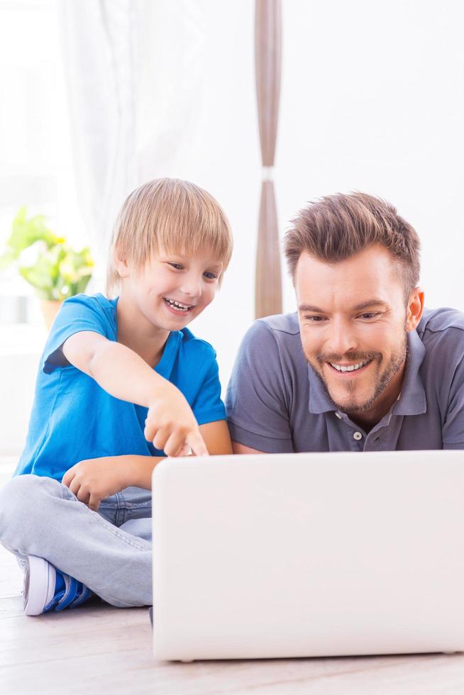 Spending time together. Happy father and son surfing the net at home while little boy pointing laptop monitor and smiling photo
