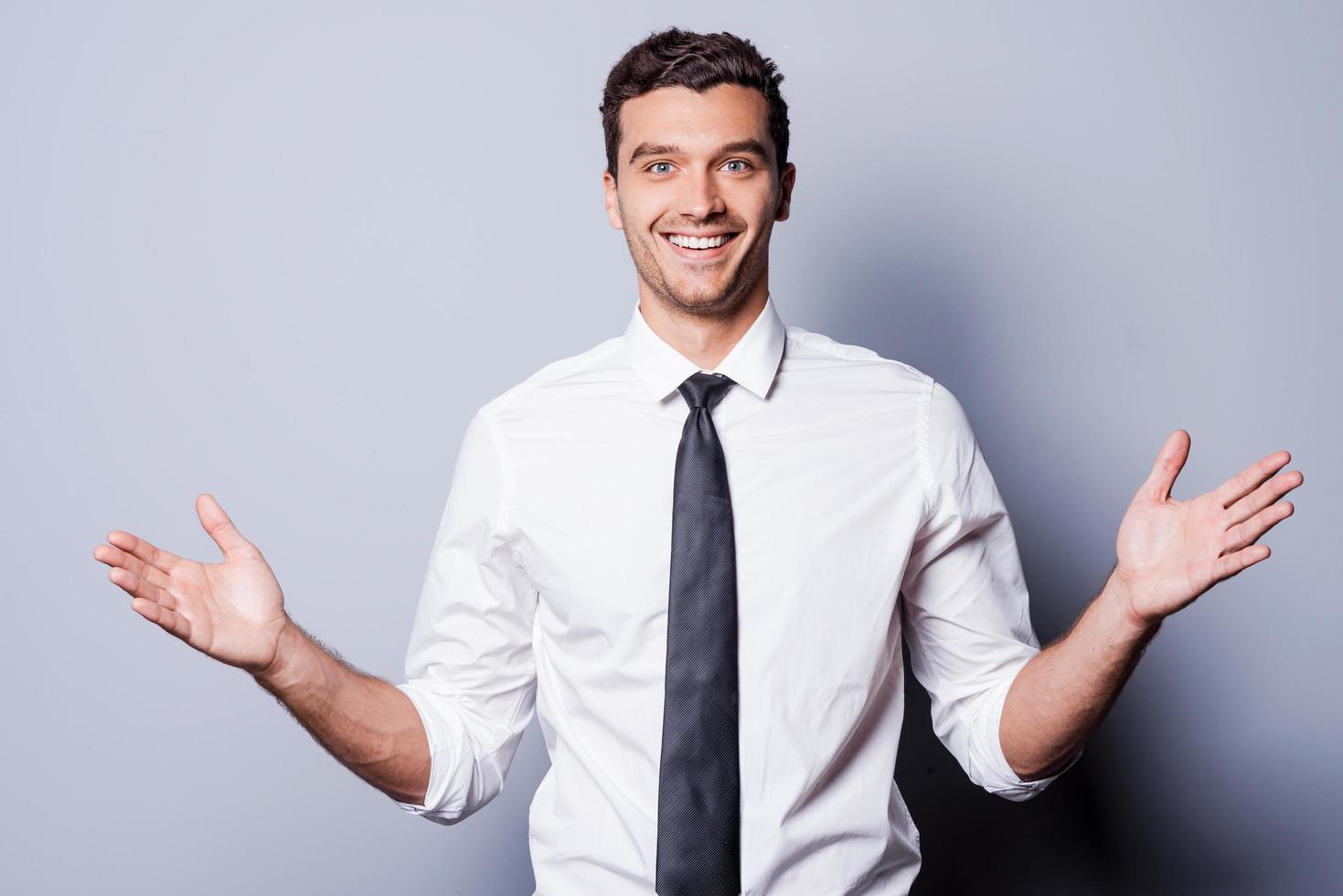 Happy businessman gesturing. Happy young man in shirt and tie gesturing and smiling while standing against grey background photo