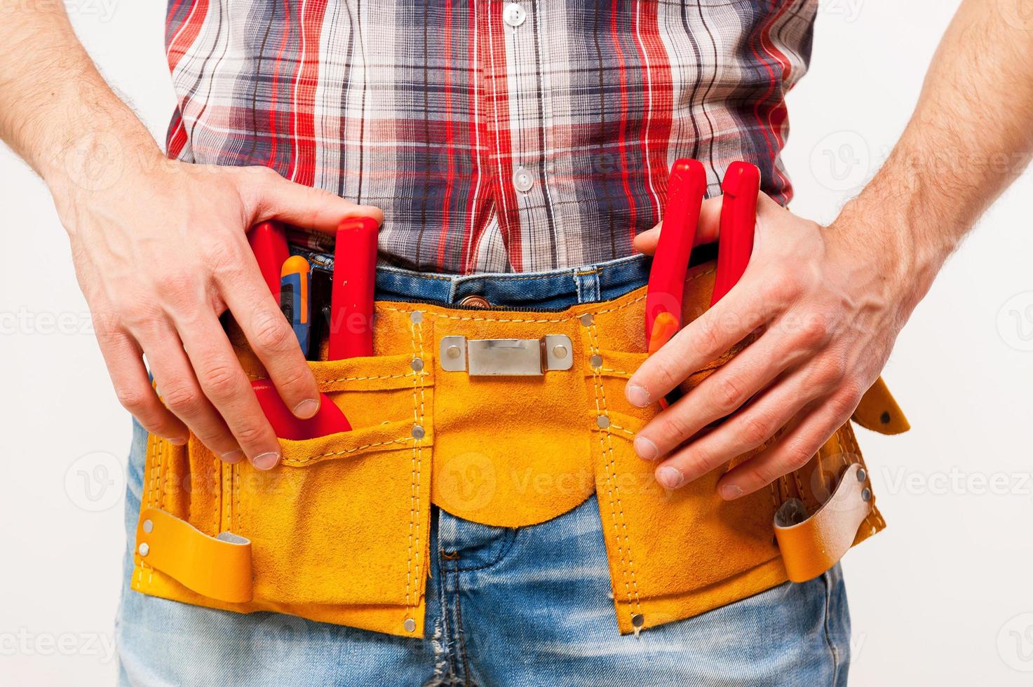Ready to work. Close-up of handyman with tool belt standing against grey background photo