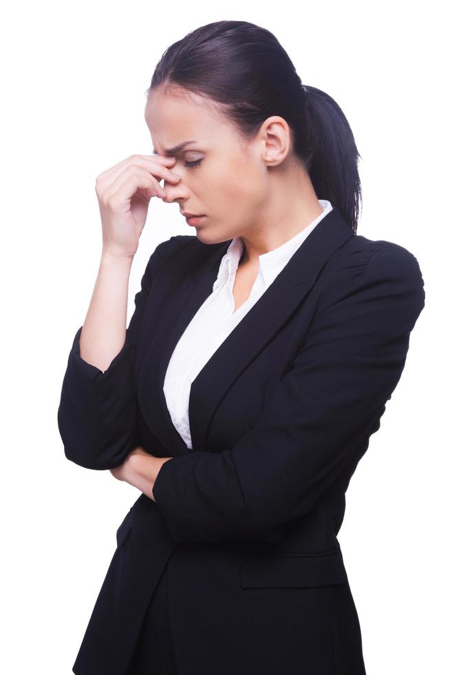 Depressed and hopeless. Side view of frustrated young woman in formalwear touching her nose and keeping eyes closed while standing isolated on white background photo