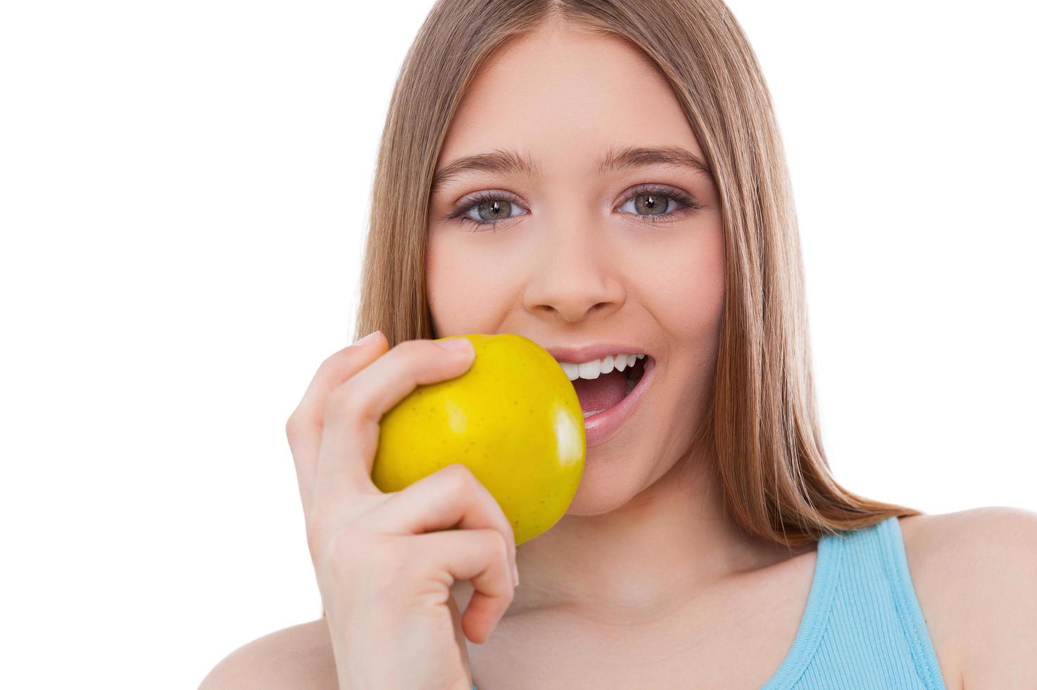 Eating a fresh apple. Cheerful teenage girl eating green apple and smiling while standing isolated on white photo