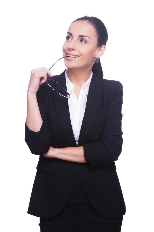 Thinking about solutions. Thoughtful young woman in formalwear carrying eyeglasses and looking away while standing isolated on white background photo