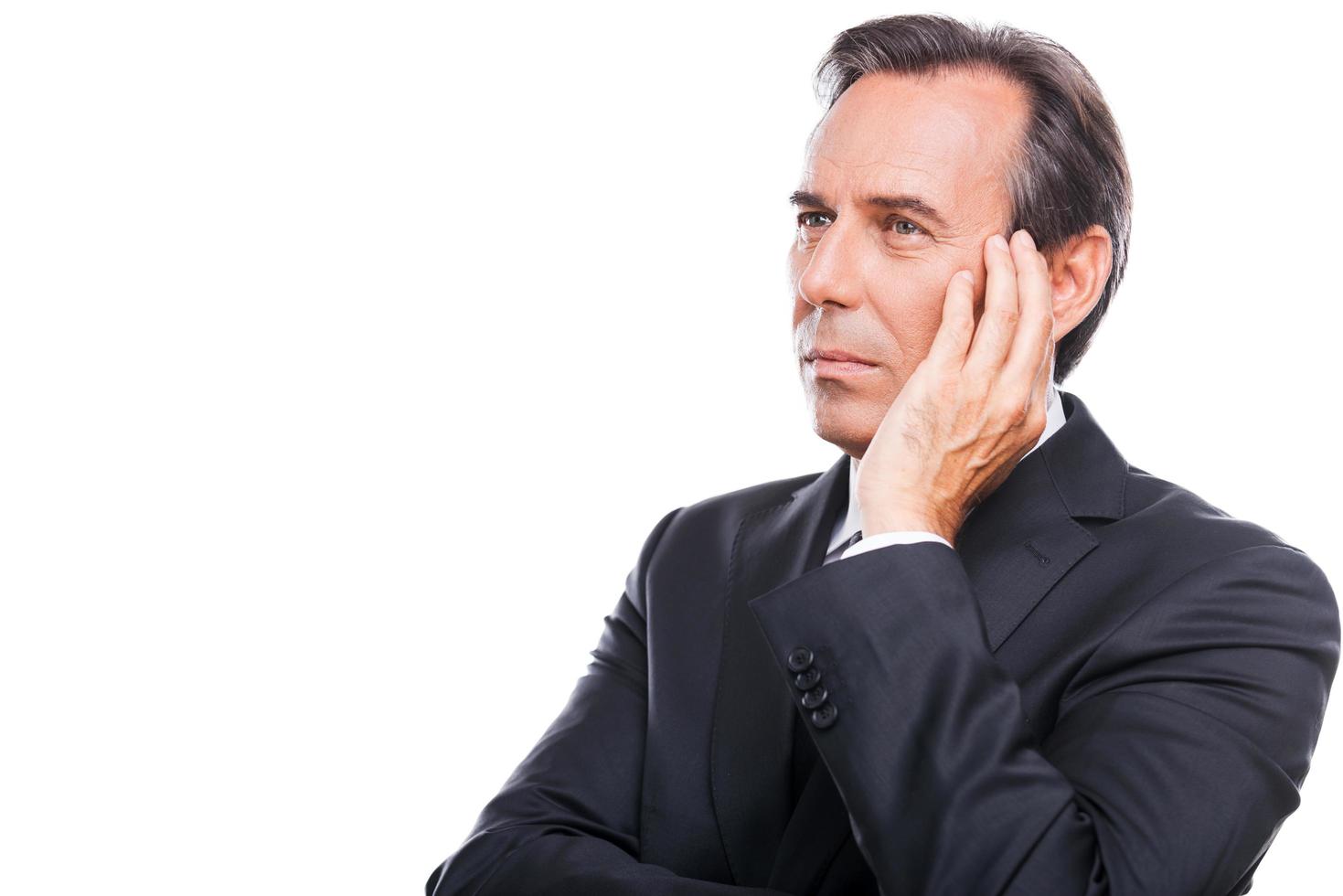 Thinking about his business future. Thoughtful mature businessman touching his face with hand and looking away while standing isolated on white background photo