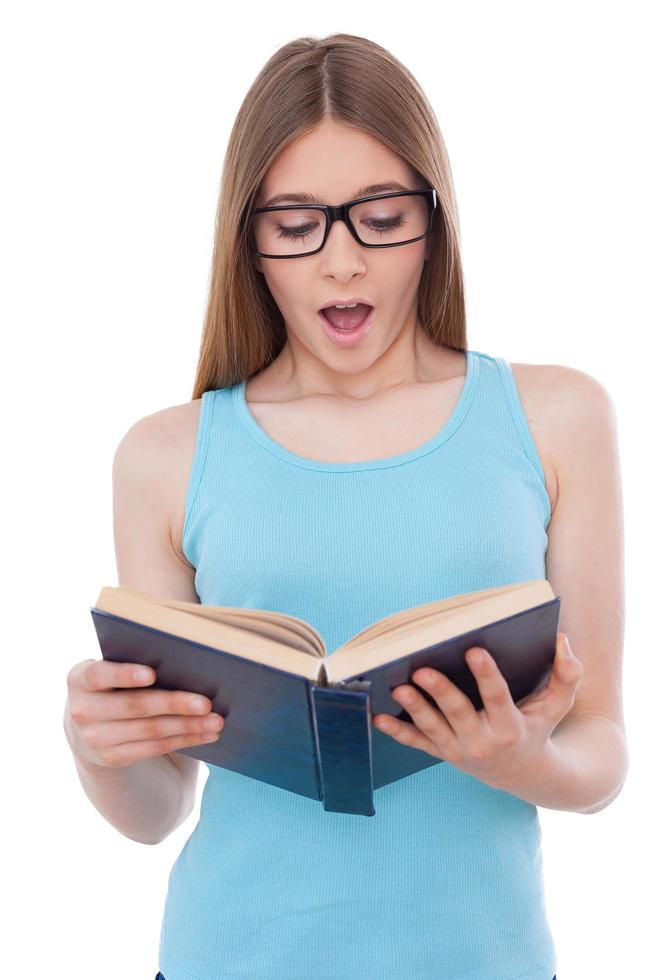 Reading an exciting book. Surprised teenage girl reading book while standing isolated on white photo