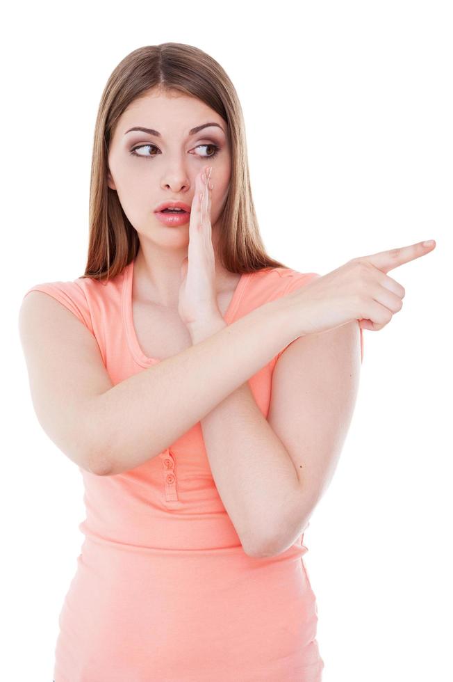 contando chismes. Atractiva mujer joven contando chismes y señalando hacia otro lado mientras está aislada en blanco foto