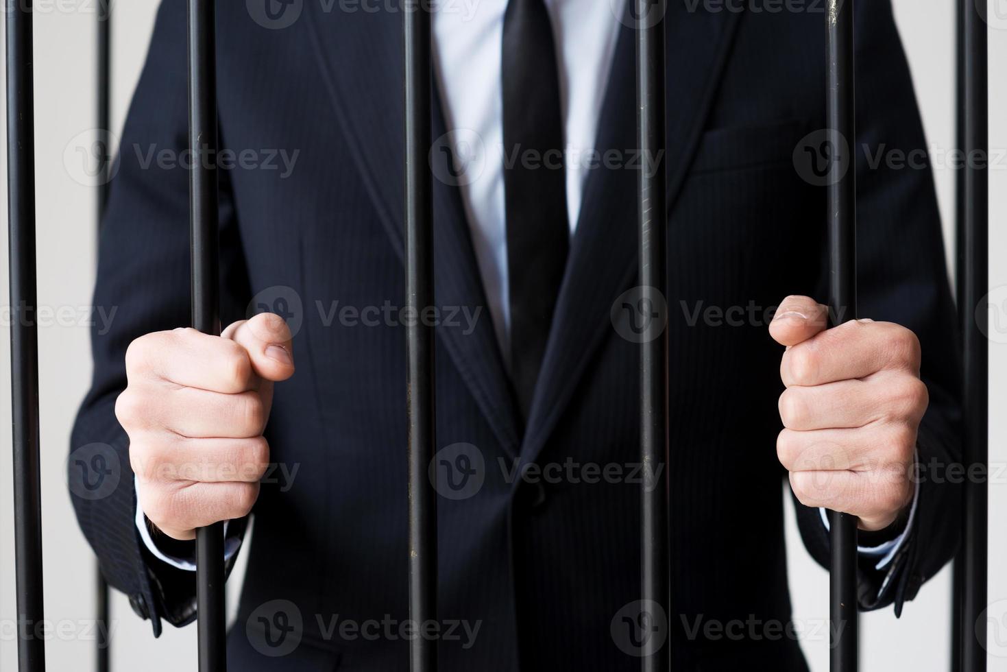 Businessmen in prison. Cropped image of man in formalwear standing behind a prison cell photo