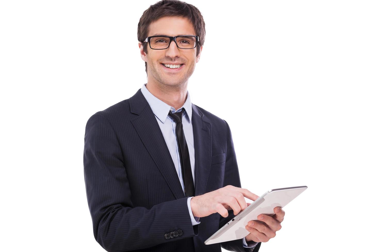 Businessman with digital tablet. Handsome young man in formalwear working on digital tablet and smiling while standing isolated on white background photo