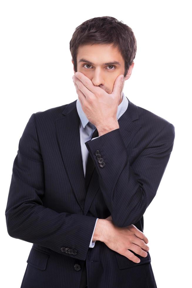 I will keep your secret. Handsome young man in formalwear covering mouth with hand and looking at camera while standing isolated on white background photo