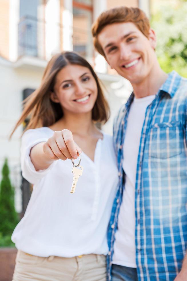 dueños de casa felices. hermosa joven pareja amorosa de pie contra la casa mientras la mujer sostiene la llave y sonríe foto