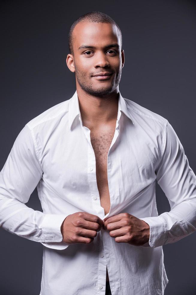 It is my favorite shirt. Handsome young black man dressing up his shirt and smiling while standing against grey background photo