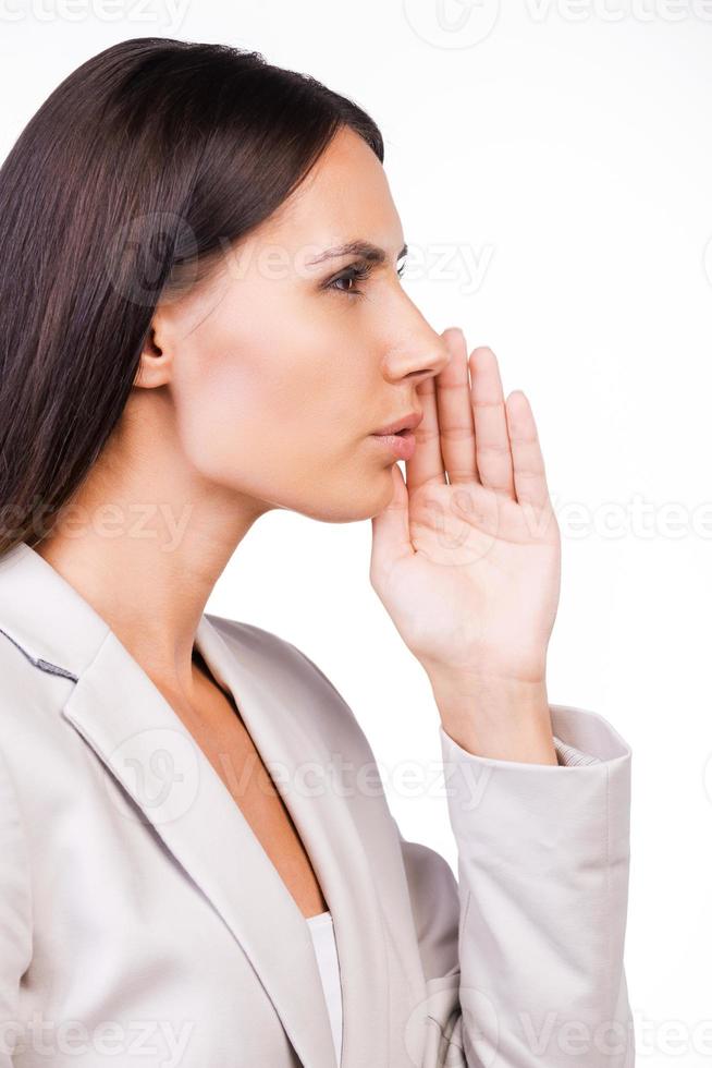 Telling fresh gossips. Side view of beautiful young businesswoman in suit telling gossips while standing against white background photo