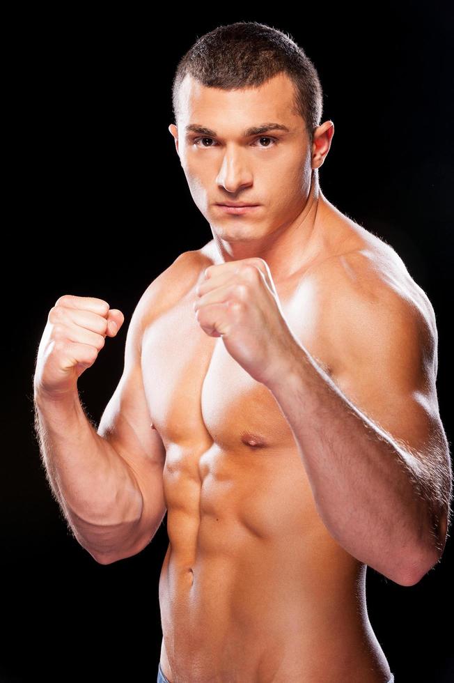 Ready to fight. Portrait of serious young shirtless man looking at camera while standing against black background photo