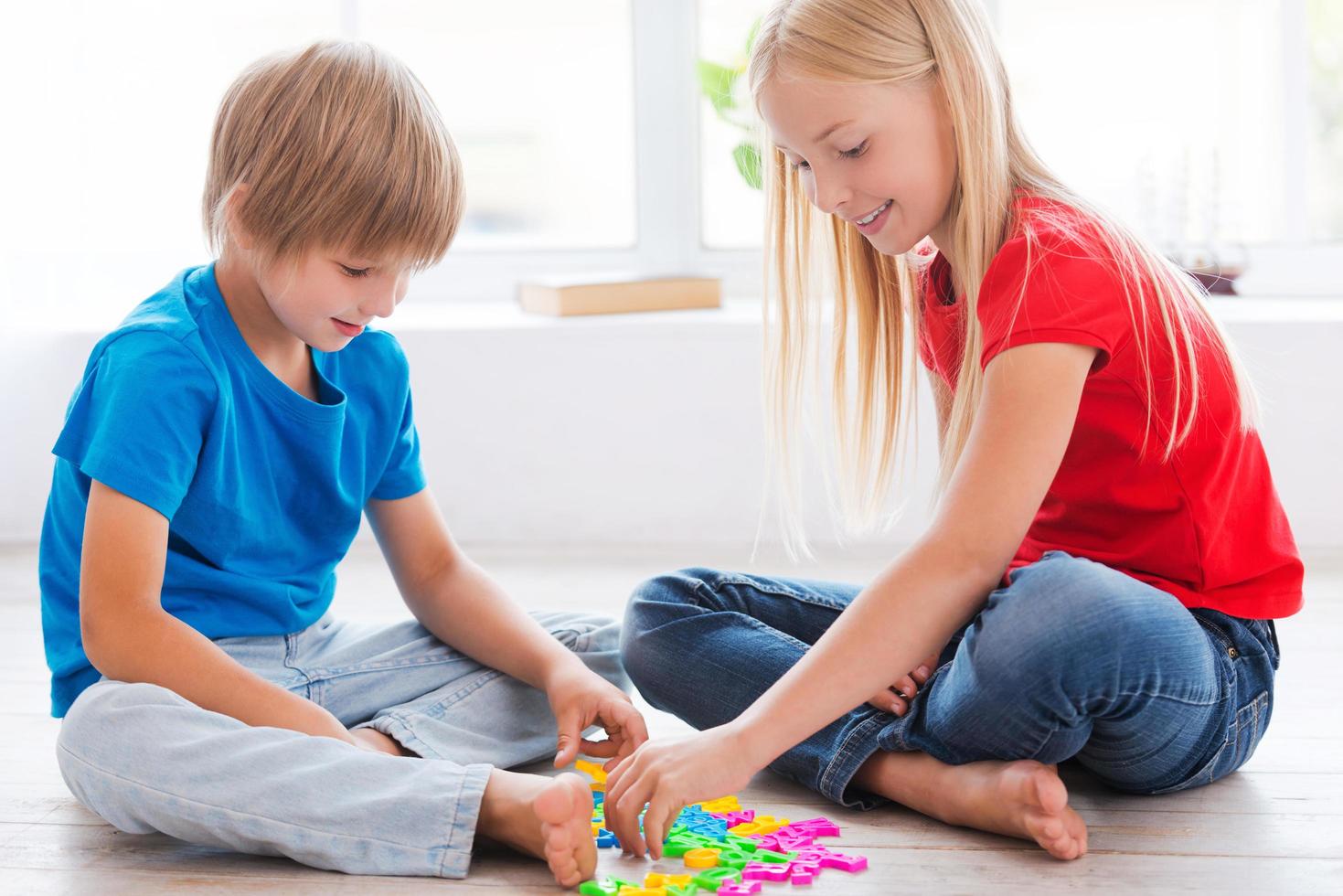 Kids playing at home. Two cute little children playing with plastic colorful letters while sitting on the hardwood floor photo