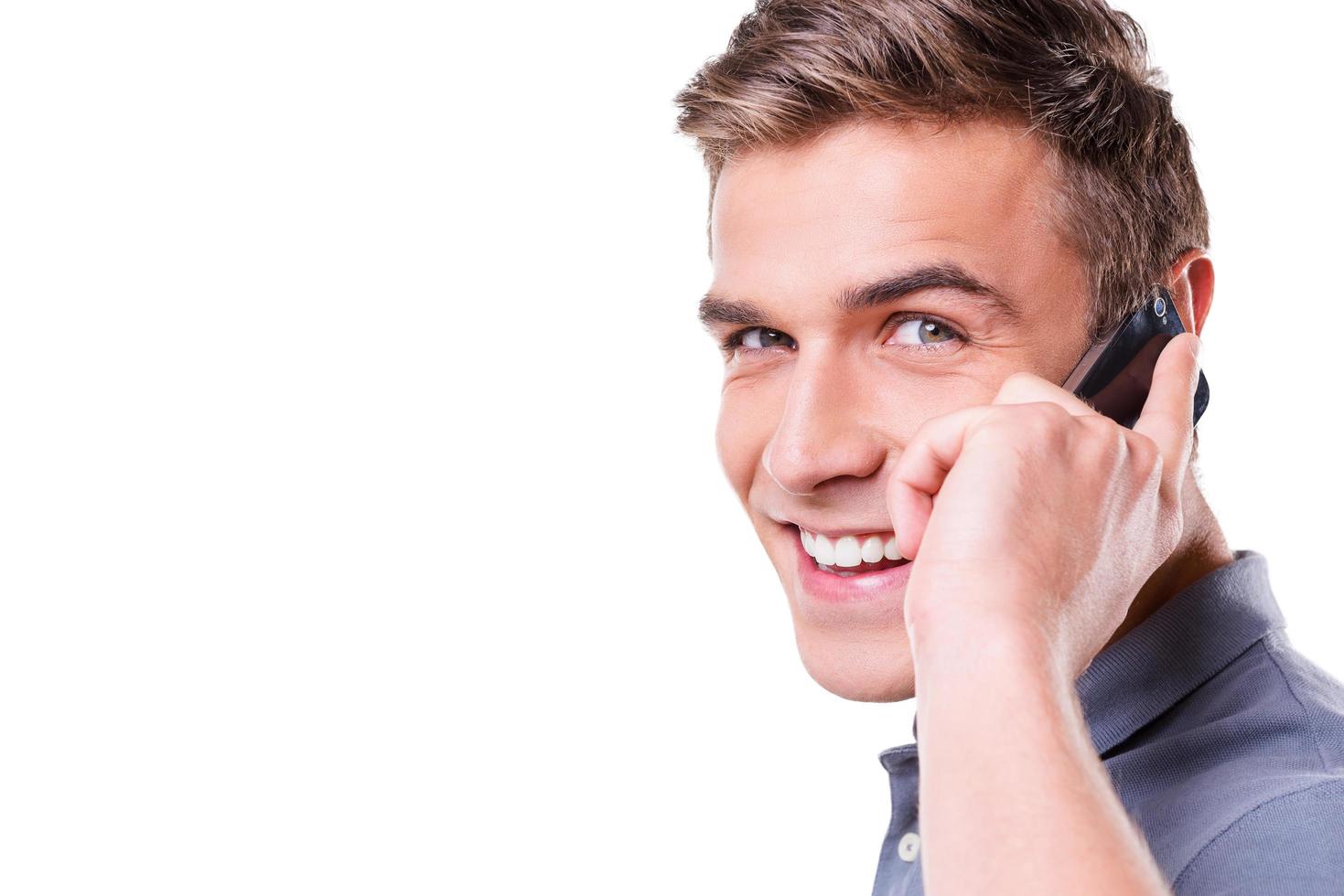 Handsome man on the phone. Happy young man talking on the mobile phone and smiling to you while standing isolated on white background photo