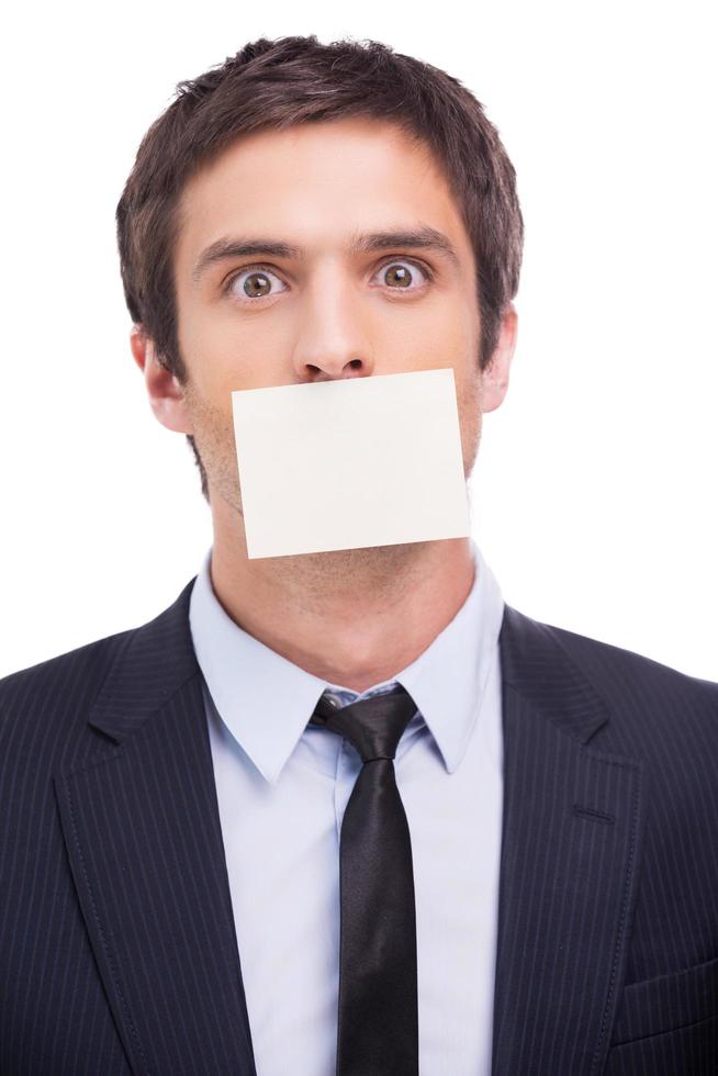 To do list. Portrait of frustrated young man in formalwear and adhesive note on his mouth standing against white background and looking at camera photo