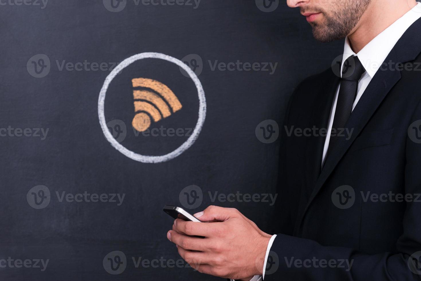 Internet connection. Close-up of young man holding telephone while standing against sharing  symbol chalk drawing on blackboard photo