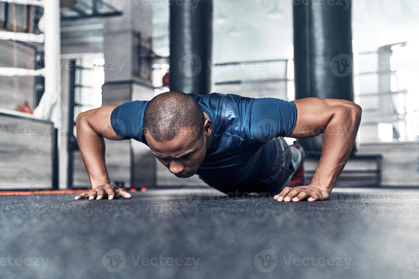 empujando fuerte apuesto joven africano con ropa deportiva haciendo flexiones mientras hace ejercicio en el gimnasio foto