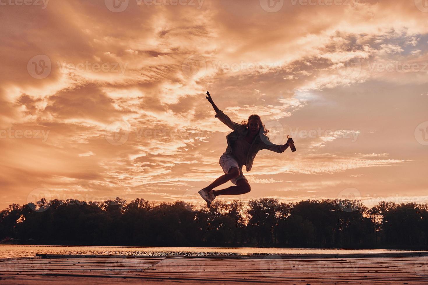 Go wild Young man hovering against dramatic sky while jumping on the pier photo